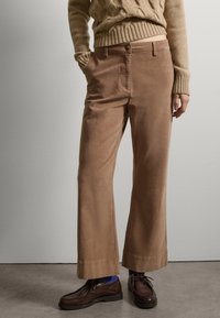 Pantalones anchos de pana marrones con una textura suave, que cuentan con un cierre frontal de botón, bolsillos laterales y un dobladillo limpio. Combinados con zapatos marrones.