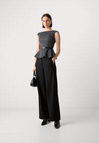 Svart høydebelte bukser kombinert med en gråstripet peplum topp med belte. Modellen holder en liten svart håndveske og har på seg svarte høye hæler.