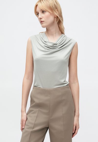 Top senza maniche con collo a cowl in tessuto grigio chiaro, caratterizzato da morbide pieghe. Abbinato a pantaloni beige a vita alta con una superficie liscia.