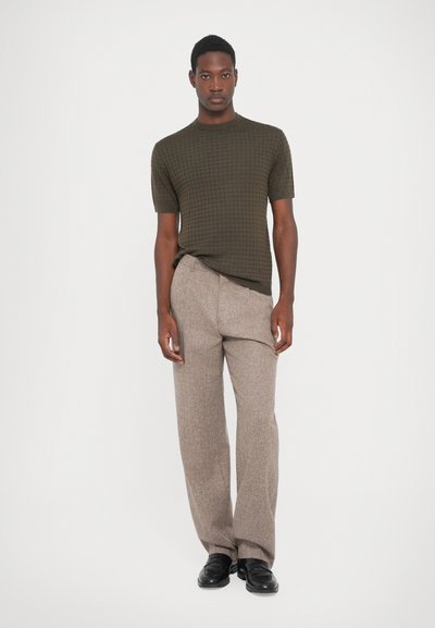 Olivgrön kortärmad texturerad skjorta med rutmönster, parat med taupe rutiga byxor. Svarta skor fulländar outfiten.