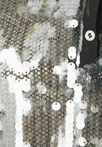 Tessuto di paillettes argento e bianche con uno sfondo in rete nera, superficie testurizzata e una patta con bottoni visibile nella parte superiore.