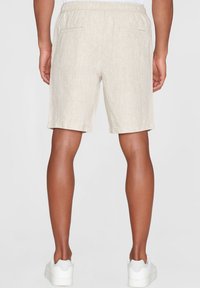 Beige linnenbyxor med elastisk midja, med två bakfickor och en avslappnad passform. Bärs tillsammans med vita sneakers.