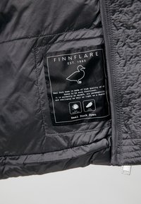 L'interno della giacca nera presenta un tessuto texturizzato con un'etichetta riportante la scritta "FINNFLARE", con dettagli sul materiale e le istruzioni di cura in testo bianco.