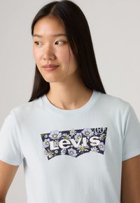 Ανοιχτό μπλε βαμβακερό t-shirt με λουλουδάτο λογότυπο Levi's σε λευκό και ναυτικό μπλε, με μπλε και κίτρινα λουλούδια σε καμπυλωτό φόντο.