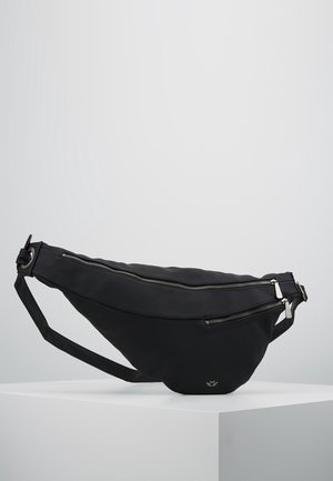 Sort crossbody-taske i stof med justerbar rem, to sølv lynlåslommer og lille logo på forsiden, vist på en hvid platform.