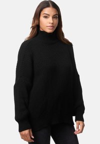 Schwarzer, gestrickter Rollkragenpullover mit lockerer Passform, strukturiertem Muster und überschnittenen Schultern, kombiniert mit dunklen Jeans.