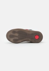 Suela de zapato con un material de goma marrón texturizado. Presenta un acento rojo redondo y un diseño de agarre con patrones para mayor tracción.