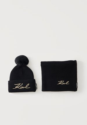 Sort strikket hue med pompom og matchende halsvarmer, begge broderet med navnet "Karl" i beige tråd.