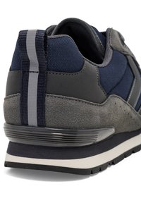 Marinblå och grå sneaker med en strukturerad ovandel, mockadetaljer, stödjande häl och en vit mellansula med gummisula.