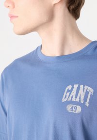 SvJetlo modra majica s kratkimi rokavi iz bombaža, ki ima na levem področju prsnega koša bledikavo belo grafiko z napisom "GANT 49".