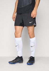 Zwarte Nike-shorts en -trui, witte Nike-sokken en zwart-blauwe voetbalschoenen. Prominente Nike-logo's op de sokken en schoenen.