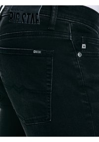 Közeli kép fekete farmer nadrág hátsó zsebéből, amelyen a "BIG STAR" márkajelzés és a varrás részletei láthatók.