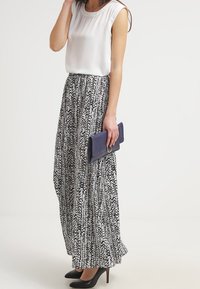 Maxikjol i svart och vitt abstrakt mönster, kombinerad med en ärmlös ljuskrämfärgad blus; håller i en mörkblå clutch; bär svarta klackar.