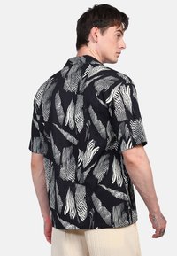 Camisa de manga corta en negro con patrones abstractos en blanco, que presenta un ajuste holgado y un diseño de cuello. Fabricada con tejido ligero y con textura.