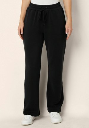 Zwarte katoenen sweatpants met een trekkoord in de taille, zijzakken, taps toelopende pijpen en een gladde textuur, gecombineerd met witte sneakers.
