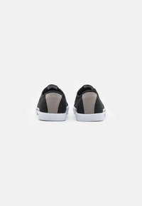 Black canvas sneakers feature a gray suede accent on the heel, white rubber sole, and textured detailing on the rear. Simple design and low-cut shape.