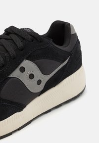 Baskets noires et grises mettant en avant une combinaison de matériaux en daim et en mesh, avec une semelle extérieure texturée et un accent logo distinctif.