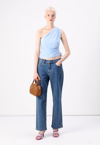 Lichtblauwe top met één schouder, gerimpeld ontwerp. Hooggewijze, losse spijkerbroek. Kleine bruine handtas met gequiltte textuur en paarse hoge hakken.