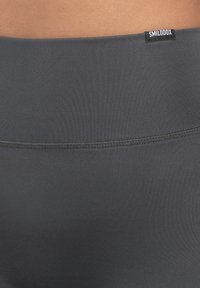 Leggings a vita alta in materiale grigio scuro, con costine testurizzate, cuciture piatte e un piccolo etichetta nera del marchio in vita.
