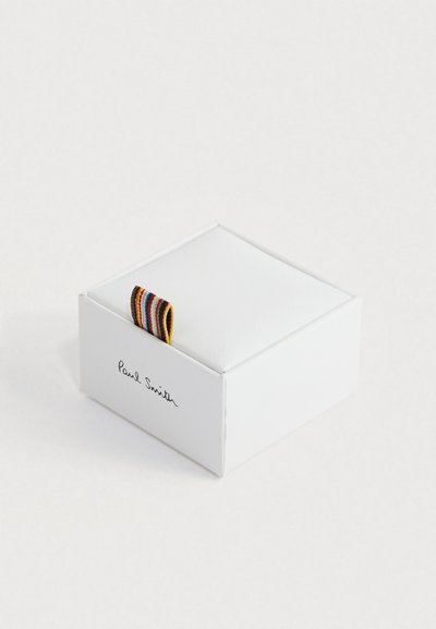 Caja blanca de la marca Paul Smith con una pequeña pestaña de tela con rayas multicolores, sobre un fondo blanco liso.