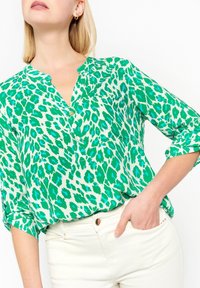 Green and white leopard-patterned blouse with three-quarter sleeves, collar, and button details, made from a smooth, lightweight fabric.