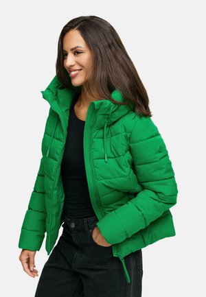 Korte groene puffy jas met capuchon, voorzien van een verticale gestikte design, rits aan de voorkant en strikkoord. Draagt over een zwarte top.