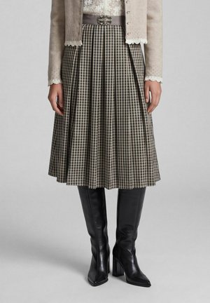 Jupe plissée à carreaux longueur genou avec motif noir et crème, associée à des bottes noires montantes à talons et une veste beige avec des manches en dentelle.