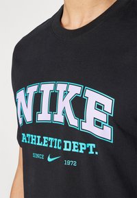 Juodas medvilninis marškinėliai su ryškiu purpuriniu "NIKE" logotipu, turkio akcentais ir užrašu "ATHLETIC DEPT." bei mažu Nike swoosh dizainu.