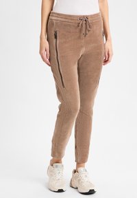 Lichtbruine corduroy joggers met zijzakken met rits, een elastische tailleband en taps toelopende enkels, gecombineerd met beige sneakers.