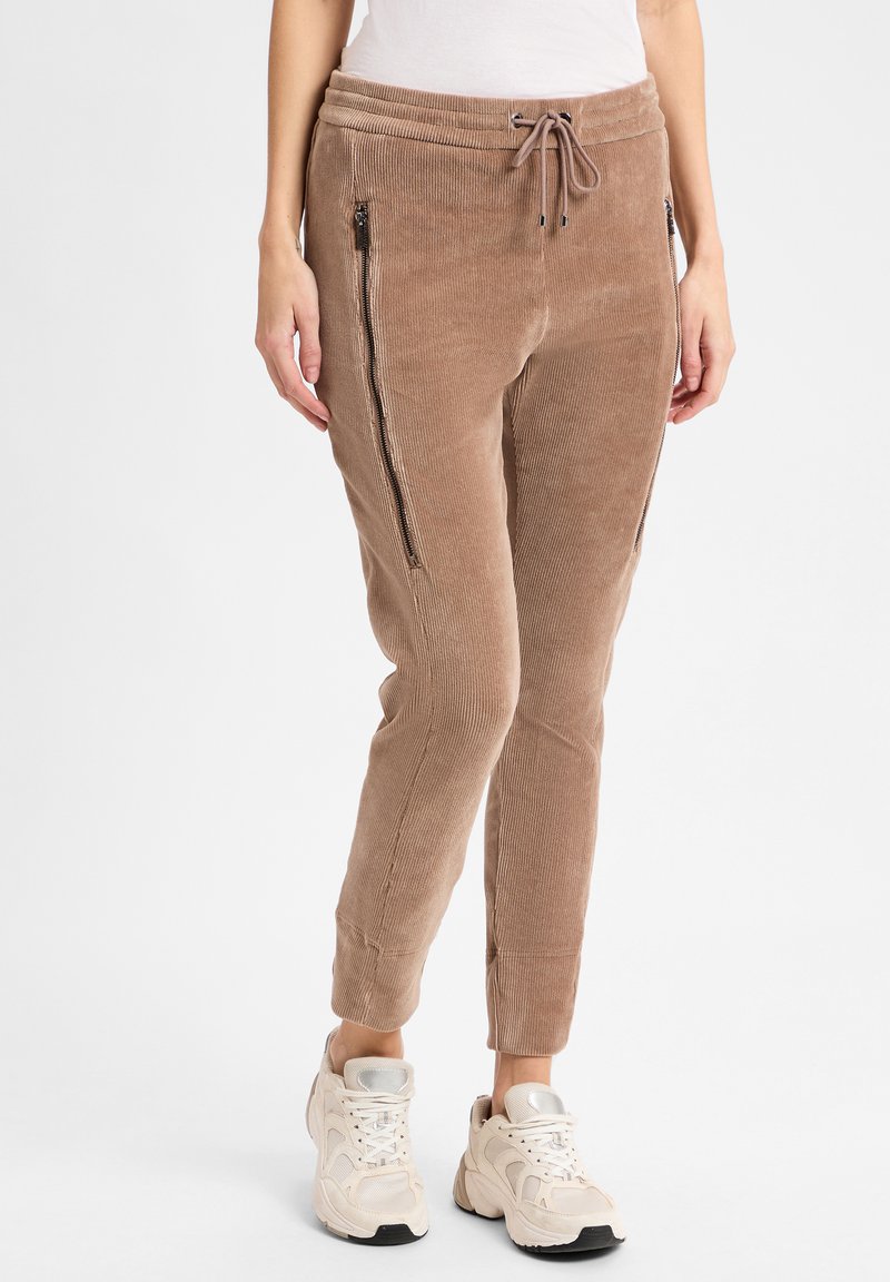 Lichtbruine corduroy joggers met zijzakken met rits, een elastische tailleband en taps toelopende enkels, gecombineerd met beige sneakers.
