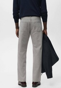 Jeans de denim gris claro con corte recto, que presentan dos bolsillos traseros y un lavado sutil, combinados con un suéter azul marino y zapatos oscuros.
