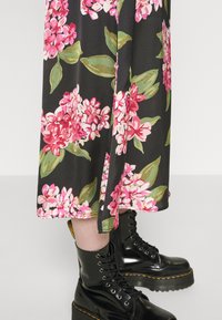 Vestido midi floral com flores rosas e brancas sobre um fundo preto, apresentando uma abertura lateral e combinado com botas de combate pretas brilhantes.