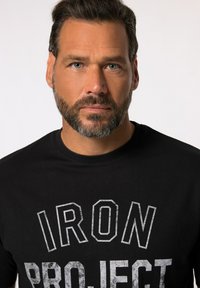 Camiseta de algodón negra con un gráfico audaz y desgastado que dice "IRON PROJECT" en letras blancas. Diseño clásico de cuello redondo.