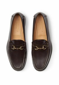 Tamno smeđi kožni mokasini s okruglim vrhom, dizajnirani s zlatnom lancem kao detaljem i ukrasnim šavovima na gornjem dijelu. Glatka tekstura.