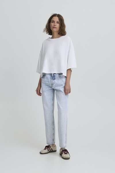 Biely skrátený tričko s širokými rukávmi, spárované so svetlomodrými džínsy s vysokým pásom a béžovými teniskami s vínovými akcentmi.