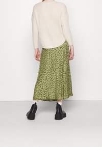 Maglione lavorato a maglia color avorio con vestibilità ampia, abbinato a una gonna midi verde con motivo floreale e stivaletti neri con suola spessa.