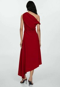 Asymmetrisches rotes Kleid mit einem kurzen Ärmel, drapiertem Stoff, fließendem Silhouette und knielangem Saum hinten. High Heels vervollständigen den Look.