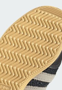 Λαστιχένια σόλα με μπεζ σχεδιασμό ζιγκ ζαγκ στο κάτω μέρος μαύρου και γκρι αθλητικού παπουτσιού για πρόσφυση και ανθεκτικότητα.