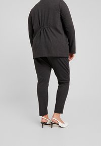 Dwuczęściowy zestaw składający się z ciemnoszarej bluzki z długim rękawem i marszczonym detalem z tyłu oraz dopasowanych spodni. Eleganckie białe buty dopełniają całość.