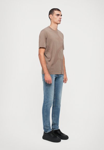 Brun strukturert t-skjorte med geometrisk design, sammen med lyseblå slim-fit jeans og svarte snørreløpesko.