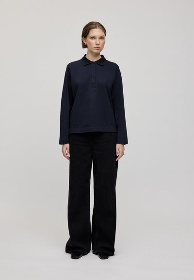 Námorní dlouhý rukáv polo s límečkem a knoflíkovou légou, spárovaný s širokými černými kalhotami. Hladká látka s minimalistickým designem.