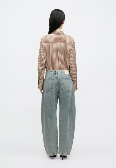 Pruunide ja beežide triipudega pikkade varrukatega särk, mis on kombineeritud hele siniste, laiade säärega teksapükstega. Sile kangas ja lõdva istuvusega disain.