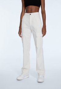 Hvide cargo bukser lavet af bomuldsstof med sidelommer, knaplukning fortil og lige ben-design. Sammen med hvide sneakers.