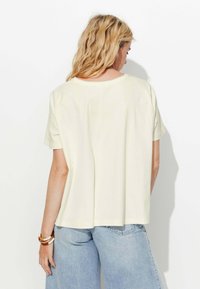 T-shirt jaune clair à manches courtes avec une coupe décontractée, présentant un col rond et un ourlet droit, associé à un jean large bleu clair.