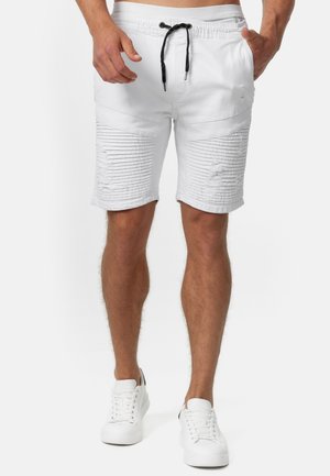 Shorts blancs avec des lignes horizontales texturées, des patchs, et une taille à cordon. Associés à des baskets blanches.