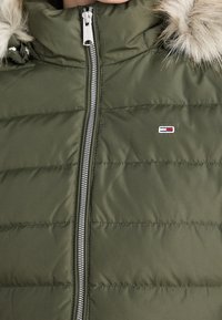 Gepolsterte olivgrüne Jacke mit einem Reißverschluss vorne, flauschiger Kapuze und kleinem Logoakzent. Leichtes Material mit gestepptem Muster.