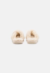 Fuzzy cream-colored slippers with a plush texture, open-toe design, and soft upper. Flat sole with a subtle tread pattern.