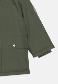 Manche d'une veste verte isolée en tissu lisse. Comprend une grande poche à rabat, une fermeture à pression et des poignets côtelés.