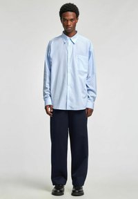 Lyseblå stripete skjorte med knapper og brystlomme, kombinert med vide marineblå bukser og svarte sko. Glatt stoff, avslappet passform.