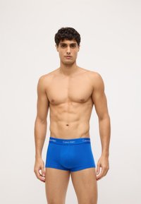 Boxeri din bumbac albastru, cu un fit strâns și o talie elastică, având un logo alb „Calvin Klein”. Textură netedă, fără modele.